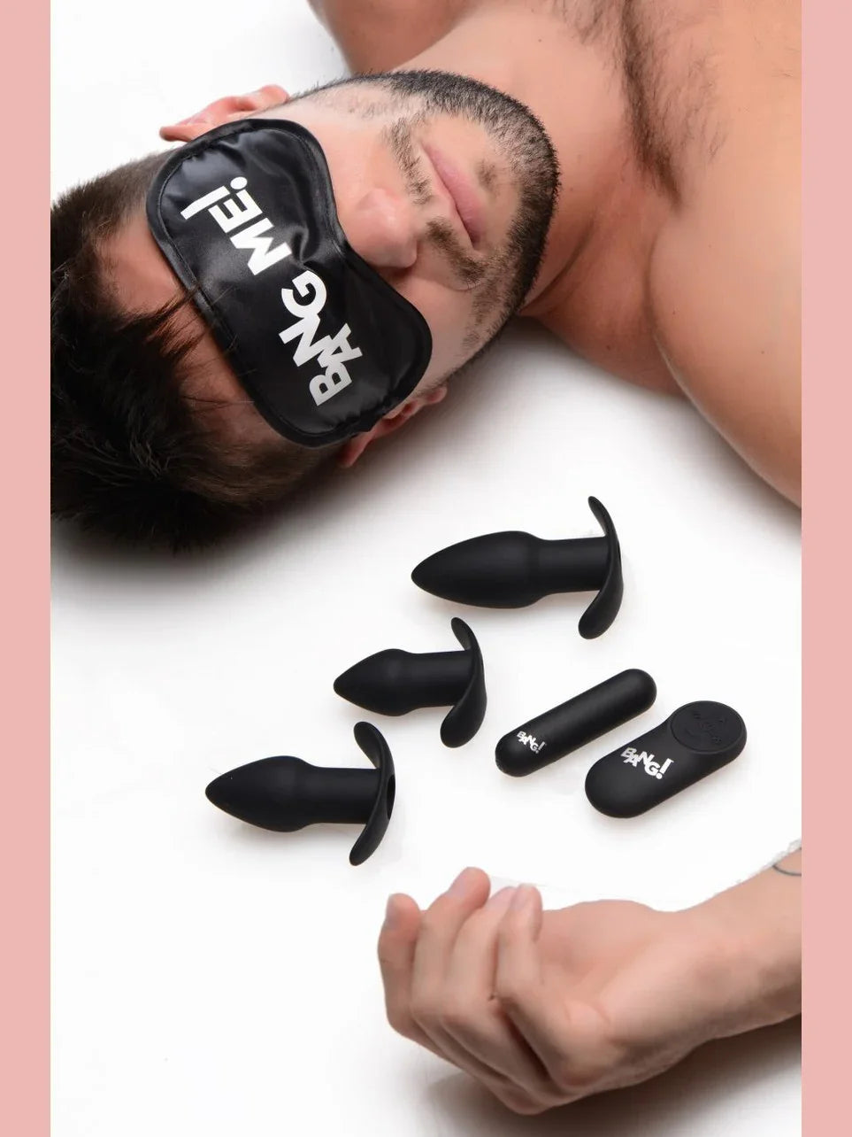Man wearing a sleep mask with 'Bang Me' text, surrounded by black silicone butt plugs on a white background.
