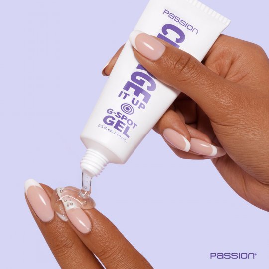 Hand applying G-Spot gel from a tube labeled 'Passion' on a light purple background.