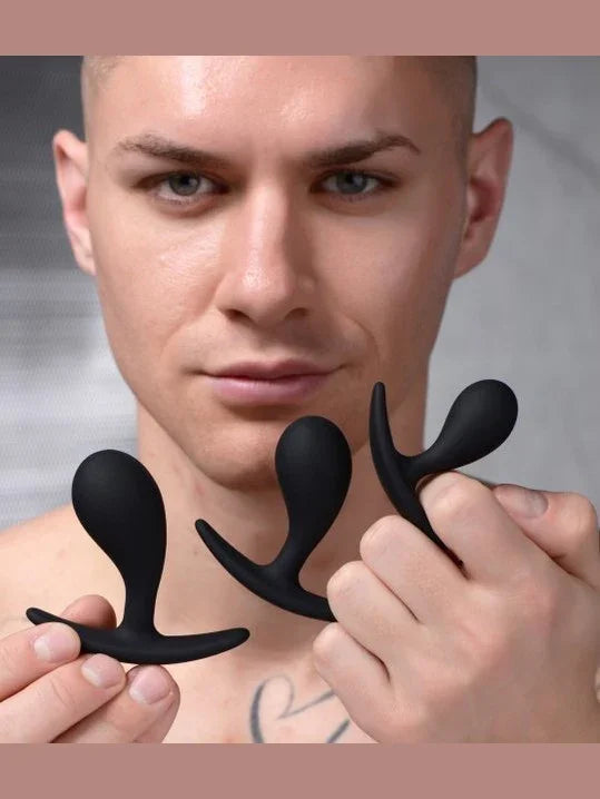Man holding two black silicone butt plugs against a neutral background
