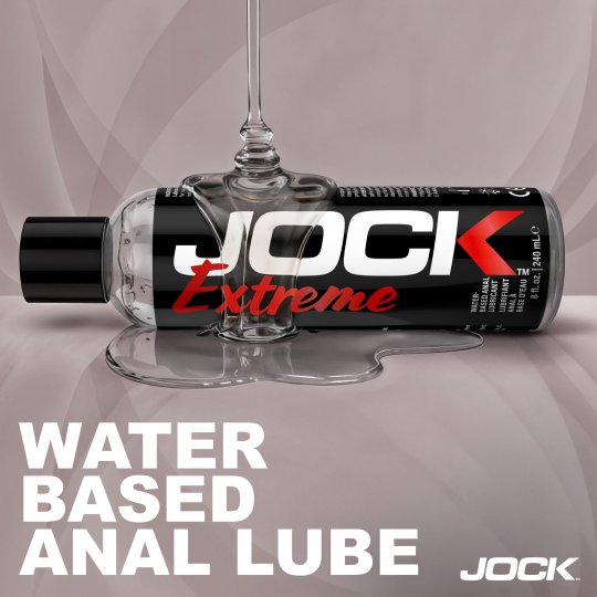 JOCK Extreme water-based anal lube bottle with a glass on a gray background