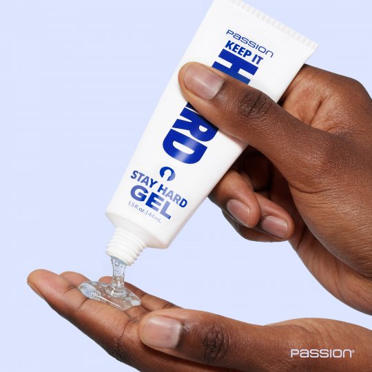 Hand holding a tube of 'Stay Hard Gel' with clear gel being squeezed out on a light blue background.