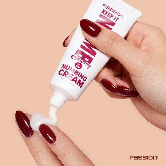 Hand holding a tube of numbing cream with visible cream being squeezed out on a beige background.