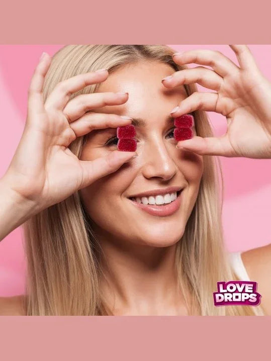 Woman holding red gummy bears over her eyes with a pink background and 'Love Drops' branding.